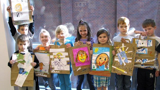 A group of children hold up artwork they created.