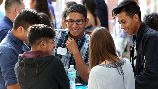 A group of Latino* students talk at a table.