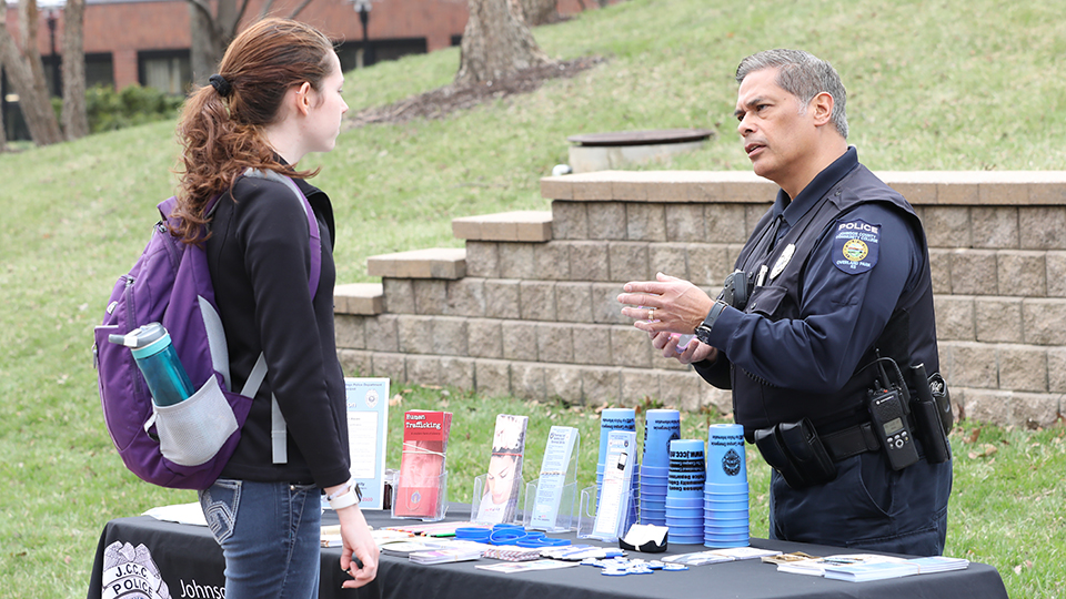 A student speaks with a JCCC Police officer at an information table.