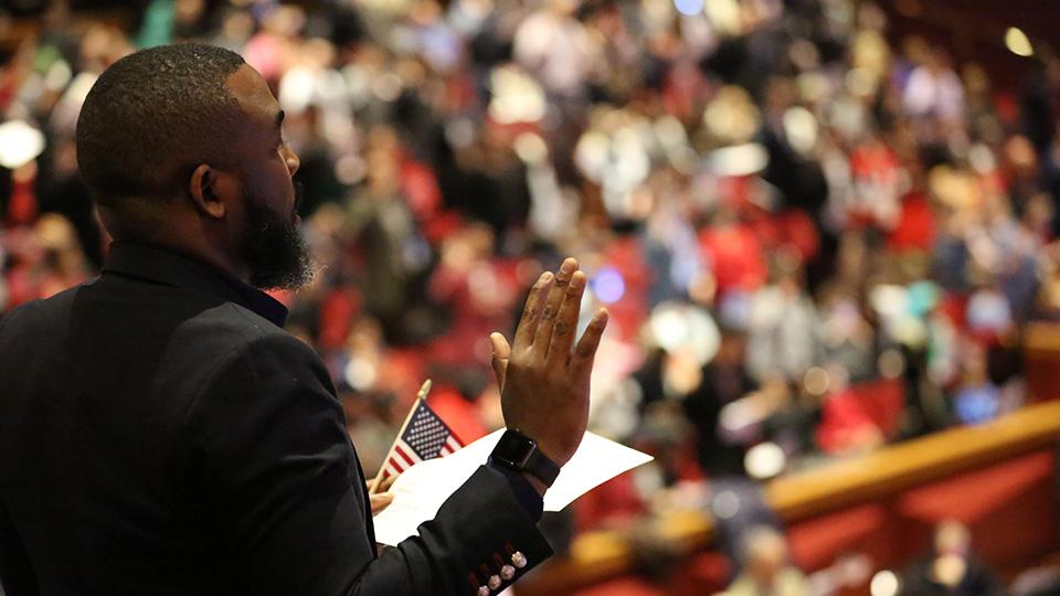An official giving the oath of citizenship to a large crowd of people