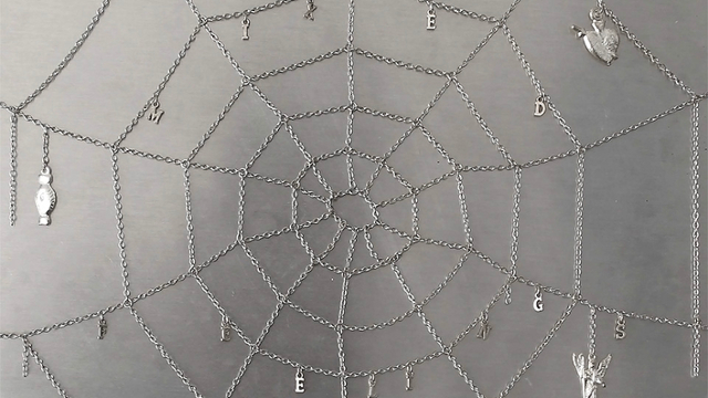 Andrew Mcilvaine, Still Haven’t Heard from You, but I’ll Wait (mixed feelings) (detail), 2023, Tin Milagros, chain, woven silver web, charms, grommets, and silver tassels attached to lowrider hoop, 27 x 17 x 2”, Courtesy the Artist.