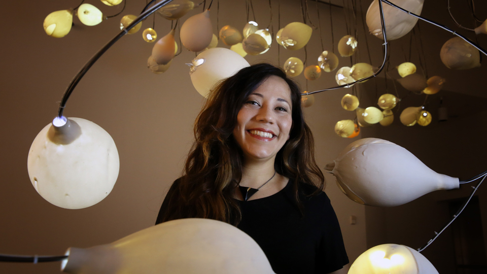 Angelica Sandoval posing with her sculpture which includes 90 L E D lightbulbs