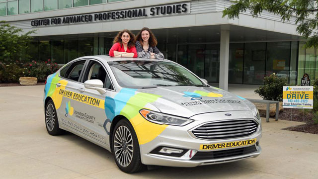 Two JCCC students posing with a car wrapped with the JCCC logo