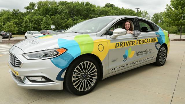 JCCC student sitting in the electric car which has the JCCC logo on it