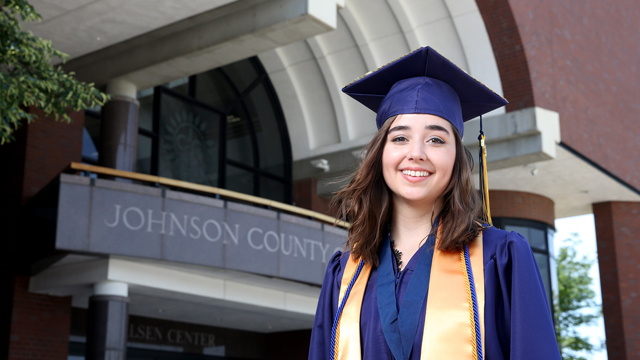 Angela Wright in her graduation cap and gown posing in front of the Carlsen Center