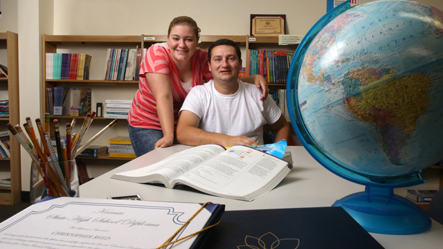 Kelcey Reed stands next to her father, Chris, who is seated at a table with an open book and a globe.