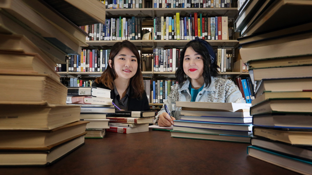 Jin Joo Hwang and Takhmina Mussayeva pose among stacks of books in the library