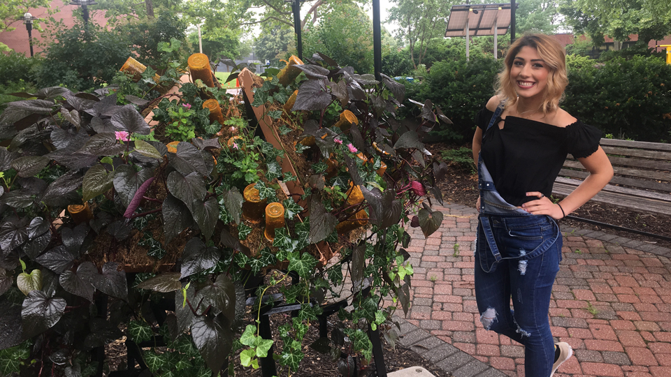 Eman Alsedeq posing with her outdoor art sculpture featuring pill bottles