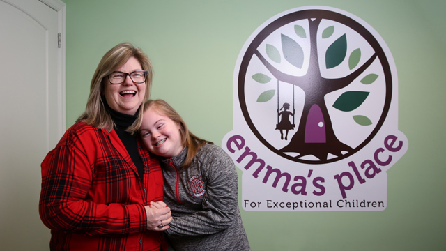 Heather Barboza poses with a day care client by the business's sign. The client is hugging heather.