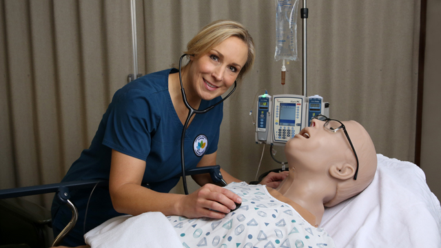 A professor demonstrates using a stethoscope on a simulation dummy