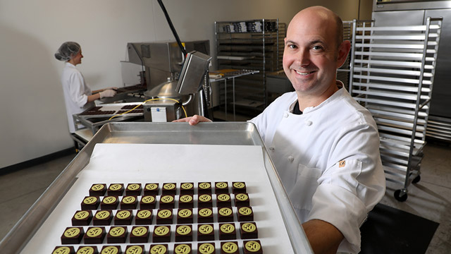 Christopher Elbow Chocolate’s Director of Production, Ethan Taylor, shows off customized JCCC 50th Anniversary chocolates.