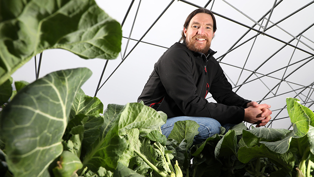 Neil Rudisill poses among plants inside his greenhouse