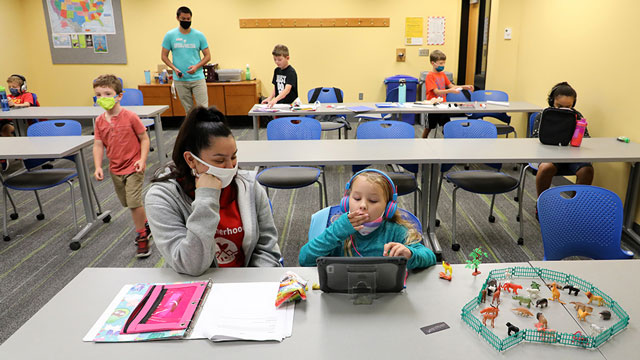 An adult sitting next to a little girl who is looking at a tablet.