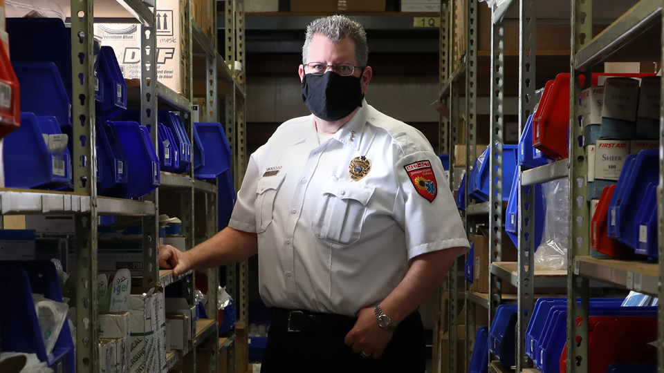 Brad Mason, wearing a mask, and standing in a storeroom of medical supplies