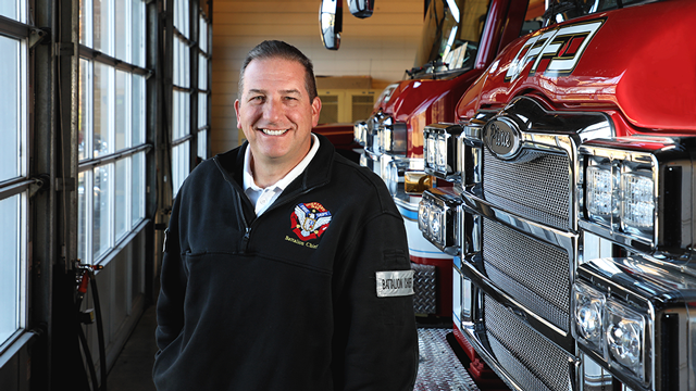 Overland Park Battalion Fire Chief Brian Redelsheimer stands in front of fire trucks.