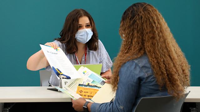 A success advocate, wearing a mask, assisting a student at the Welcome Desk