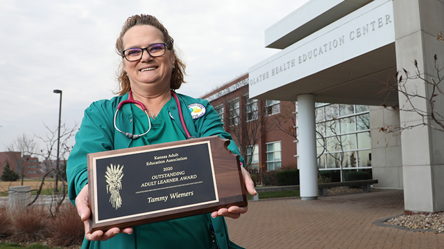 Tammy Wiemers holding her award as she stands outside the Olathe Health Education Center