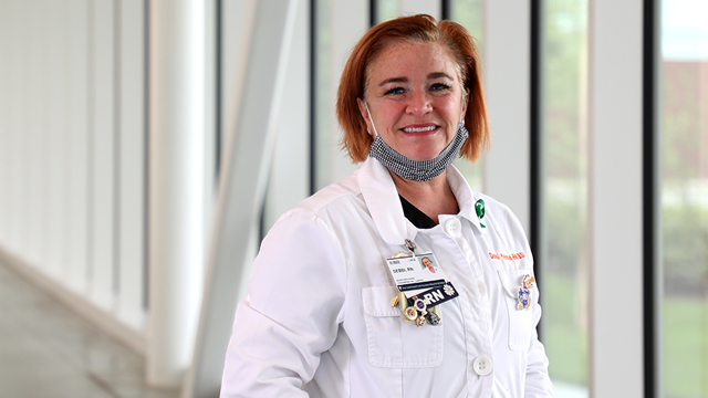 Debbi Yeoman wearing a lab coat and a face mask pulled down under her chin