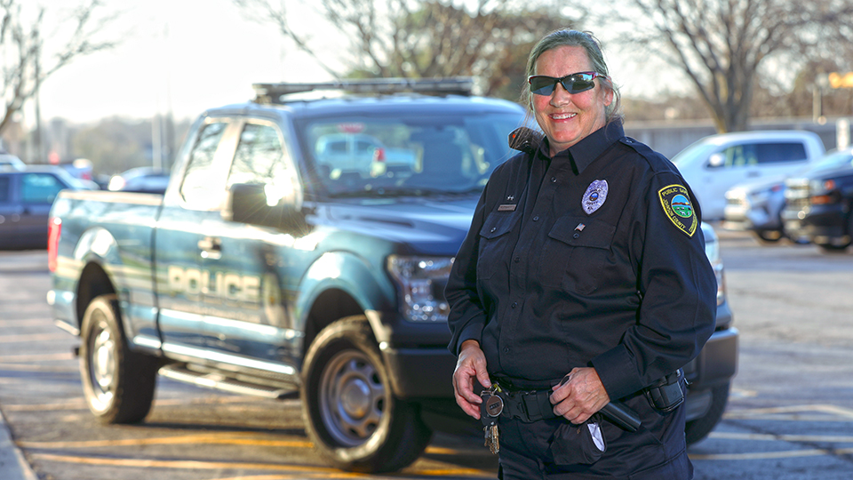 Officer Kathy Rhoades wearing her police uniform and standing in front of a police pickup truck