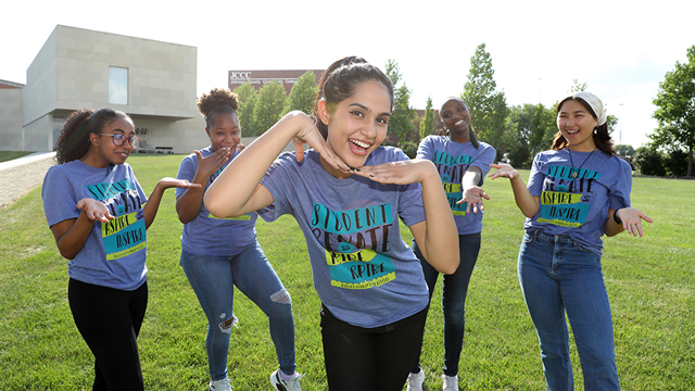 JCCC international student and Astha Thapa smiles and poses outdoors surrounded by other Student Senate members, all in matching t-shirts.