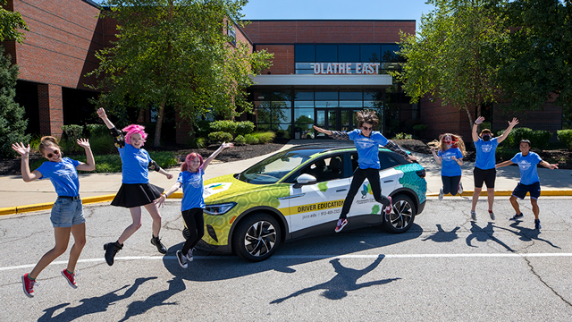 Driver's education students jumping for joy in front of an electric car