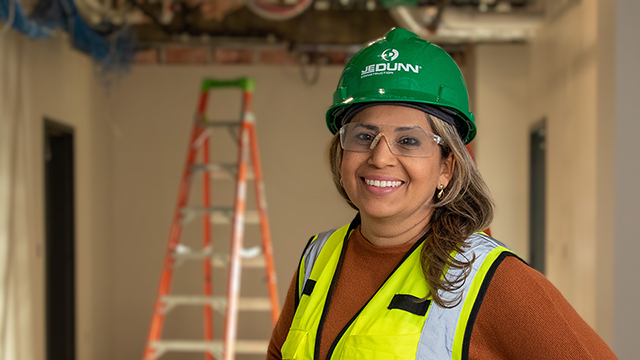 Ana Linz Perdigao in a hard hat and construction vest with a ladder in the background