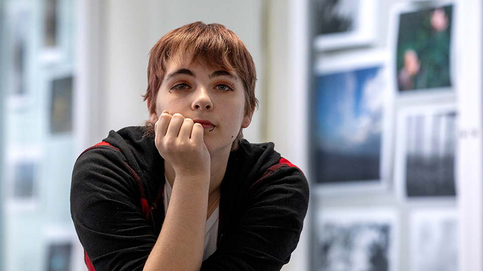 Liberty Wheatley looks at the camera, learning forward on her hand, with blurred artwork displayed on walls in the background.