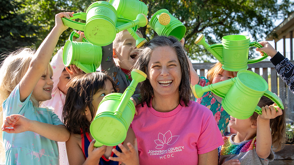 Toby surrounded by young children who are pretending to "water" her with watering cans