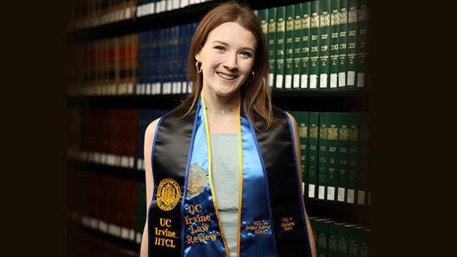 Grace Palcic wearing a graduation gown standing an a law library