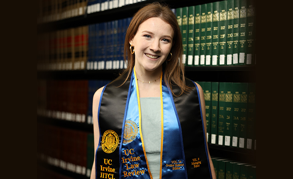 Grace Palcic wearing a graduation gown standing an a law library
