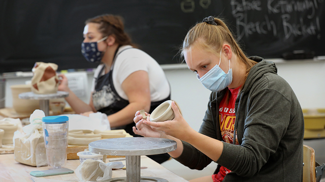 Students wearing masks working on ceramics in the studio