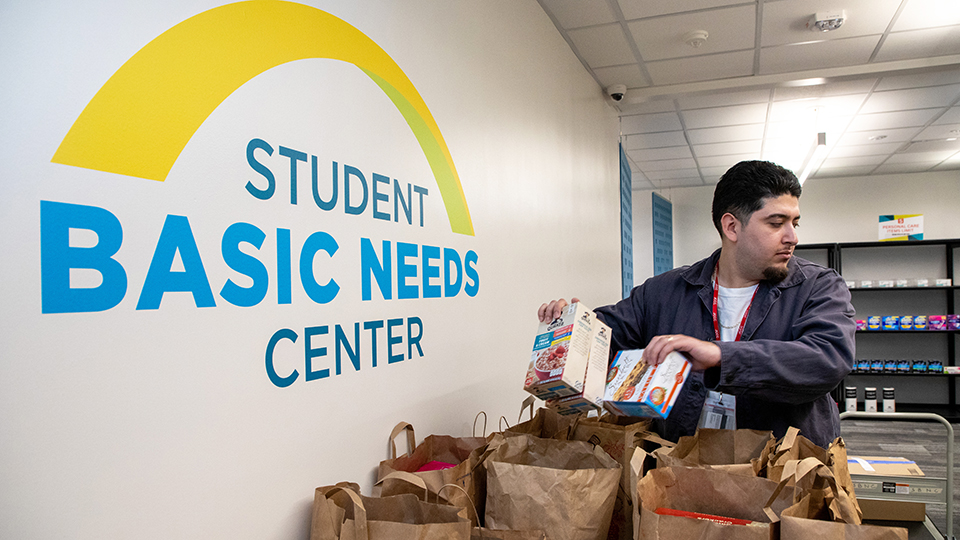 a man packs donated food into bags next to the sign for the Student Basic Needs Center