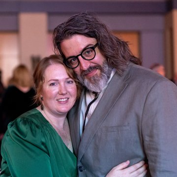 a man and woman embrace and smile at the viewer
