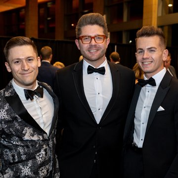 three men in tuxedoes smile at the viewer