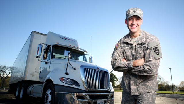 Student who is a veteran poses in camouflage uniform in front of a semi.