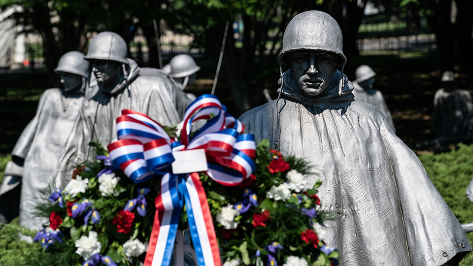 Statues of Korean War soldiers wearing helmets and rain gear - a red, white and blue wreath is in the foreground