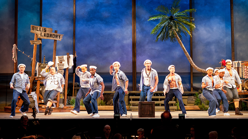 A scene from the musical South Pacific - 10 male actors singing on stage.