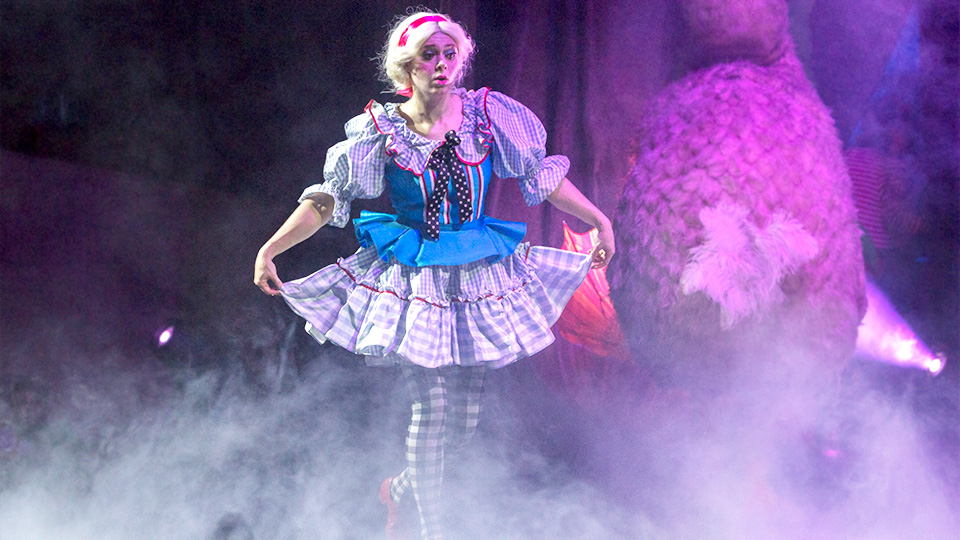 An actress portraying Alice stands on stage surrounded by thick fog.