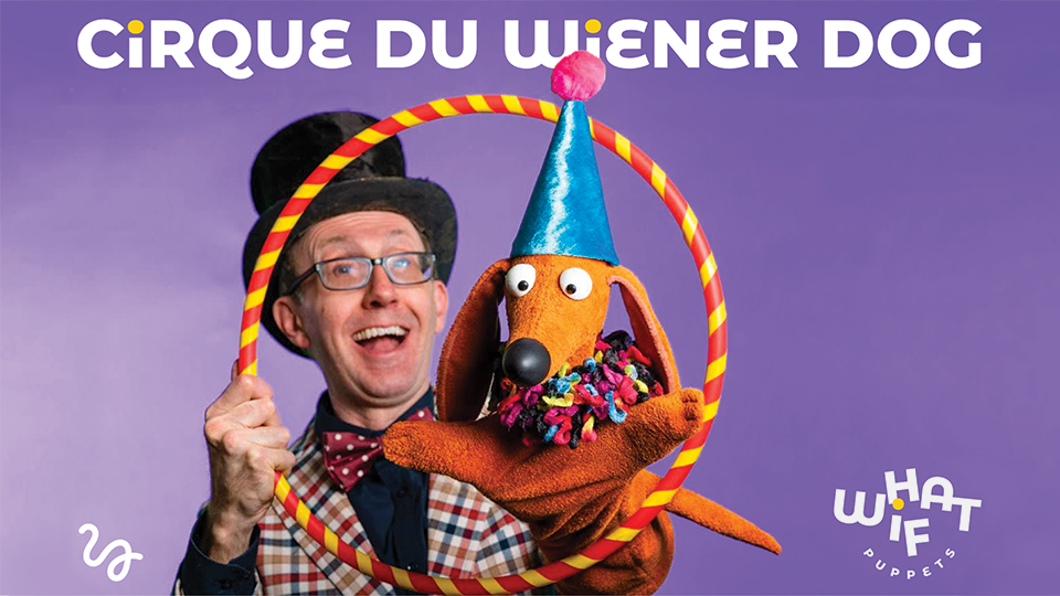 a puppeteer holding up a stuffed wiener dog and a hoop for it to jump through