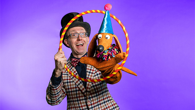 a puppeteer holding up a stuffed wiener dog and a hoop for it to jump through