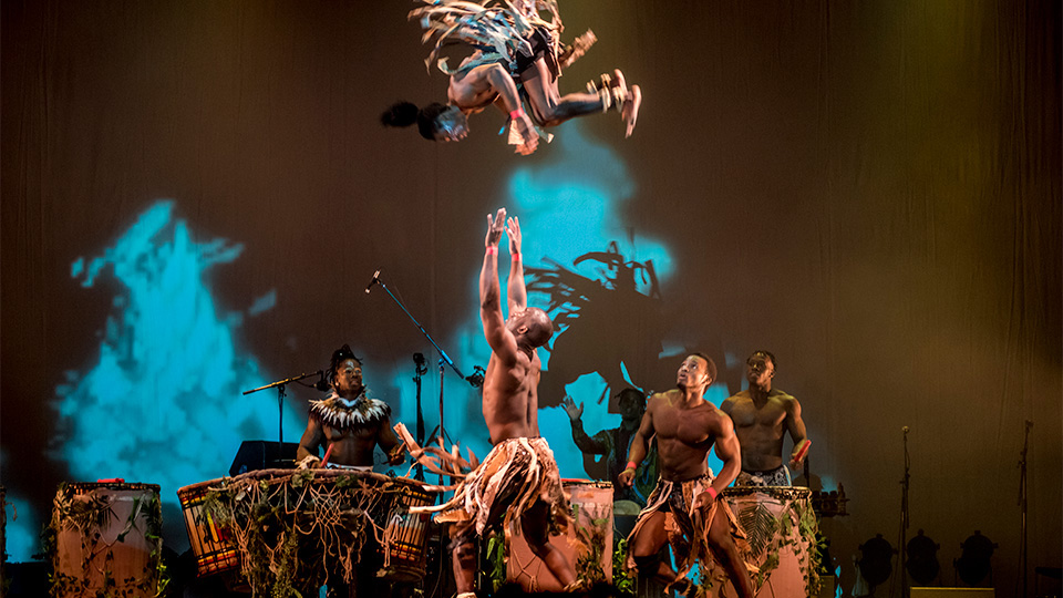 Cirque Kalabante performance, with men playing drums and another man rolling in the sky and being caught.