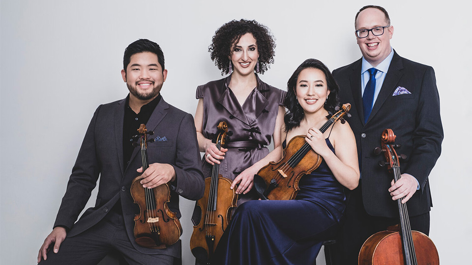 the four members of the Verona Quartet smile and look toward the camera while holding their instruments