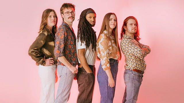 The members of Kat King stand in a line in front of a pink backdrop