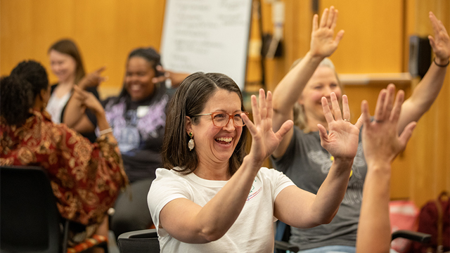 teachers in a workshop smiling and  gesturing with their hands raised