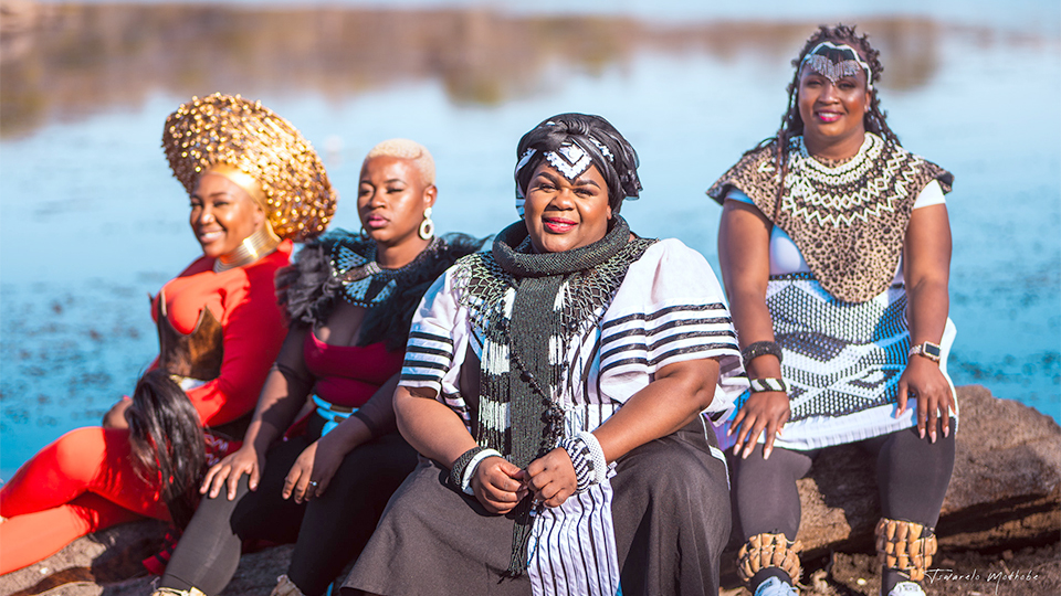 the four members of Nobuntu sitting on a rock in front of a lake.