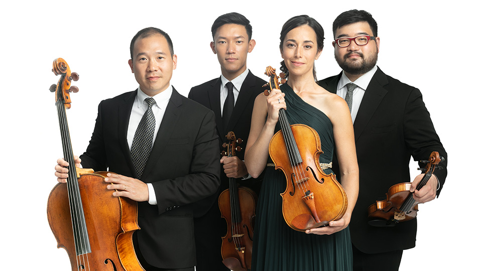 The 4 members of the Parker Quartet pose smiling at the camera while holding up their instruments