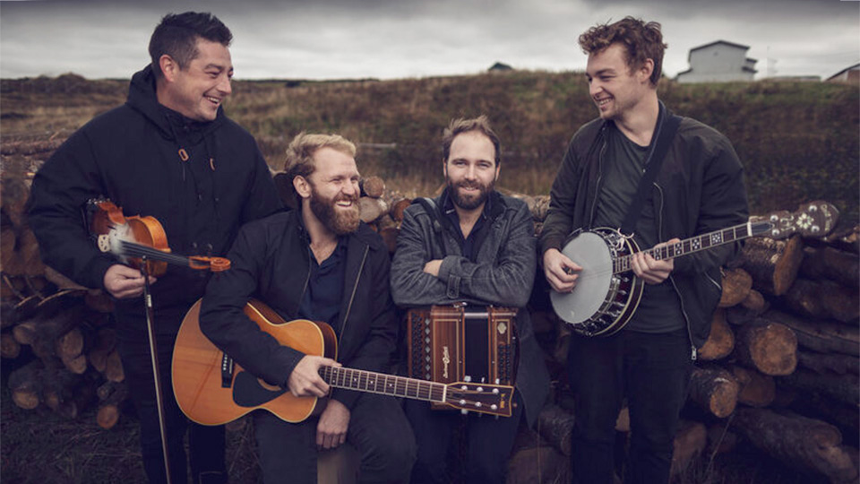 the four members of rum ragged pose for a picture with their instruments - they are outside in a rugged landscape