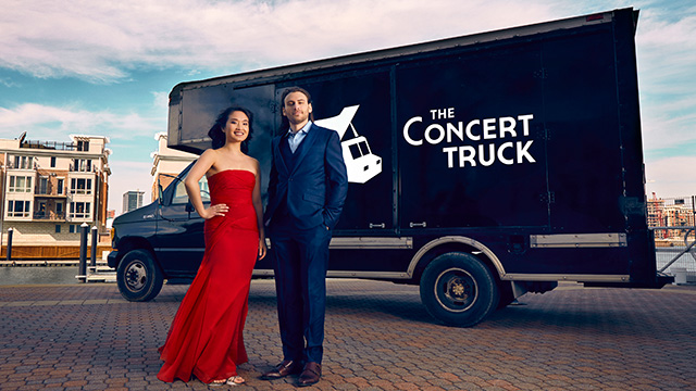 a woman in a red dress and a man in a suit stand in front of a black truck with the words the concert truck on it