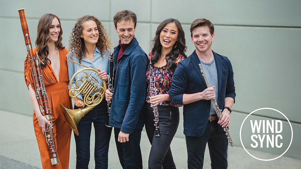 five members of windsync stand together while holding their instruments