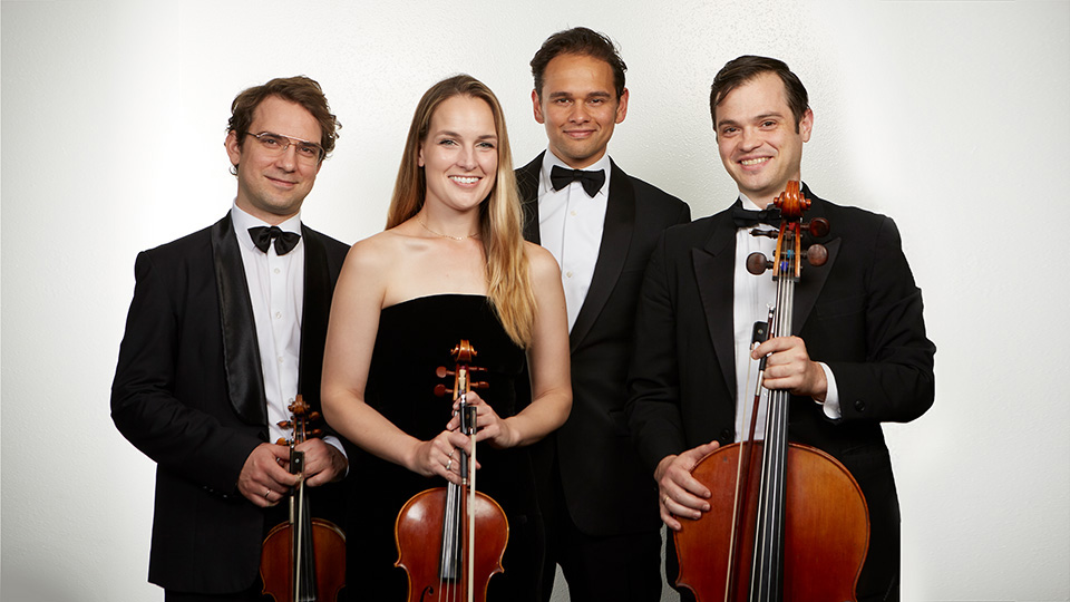 the 4 members of Opus 76 wearing black tie stand smiling at the camera while holding their instruments